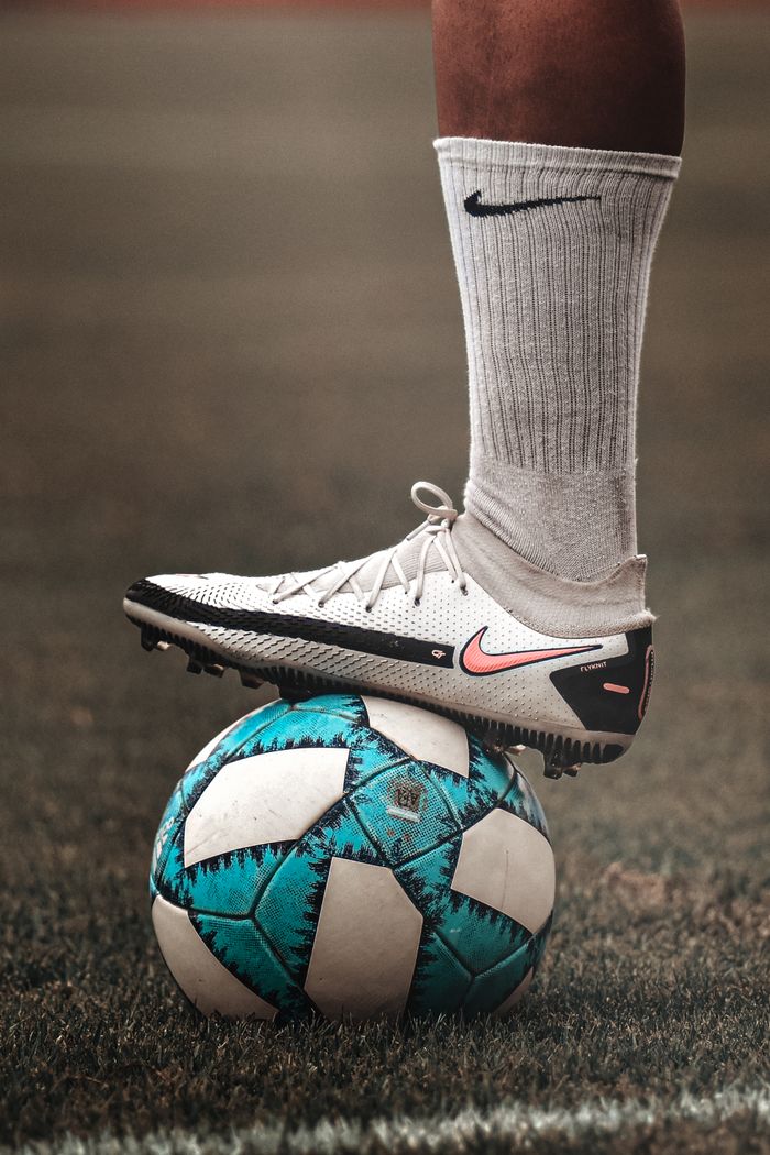 gallery-02 A person in sportswear balancing a blue soccer ball on grassy field.