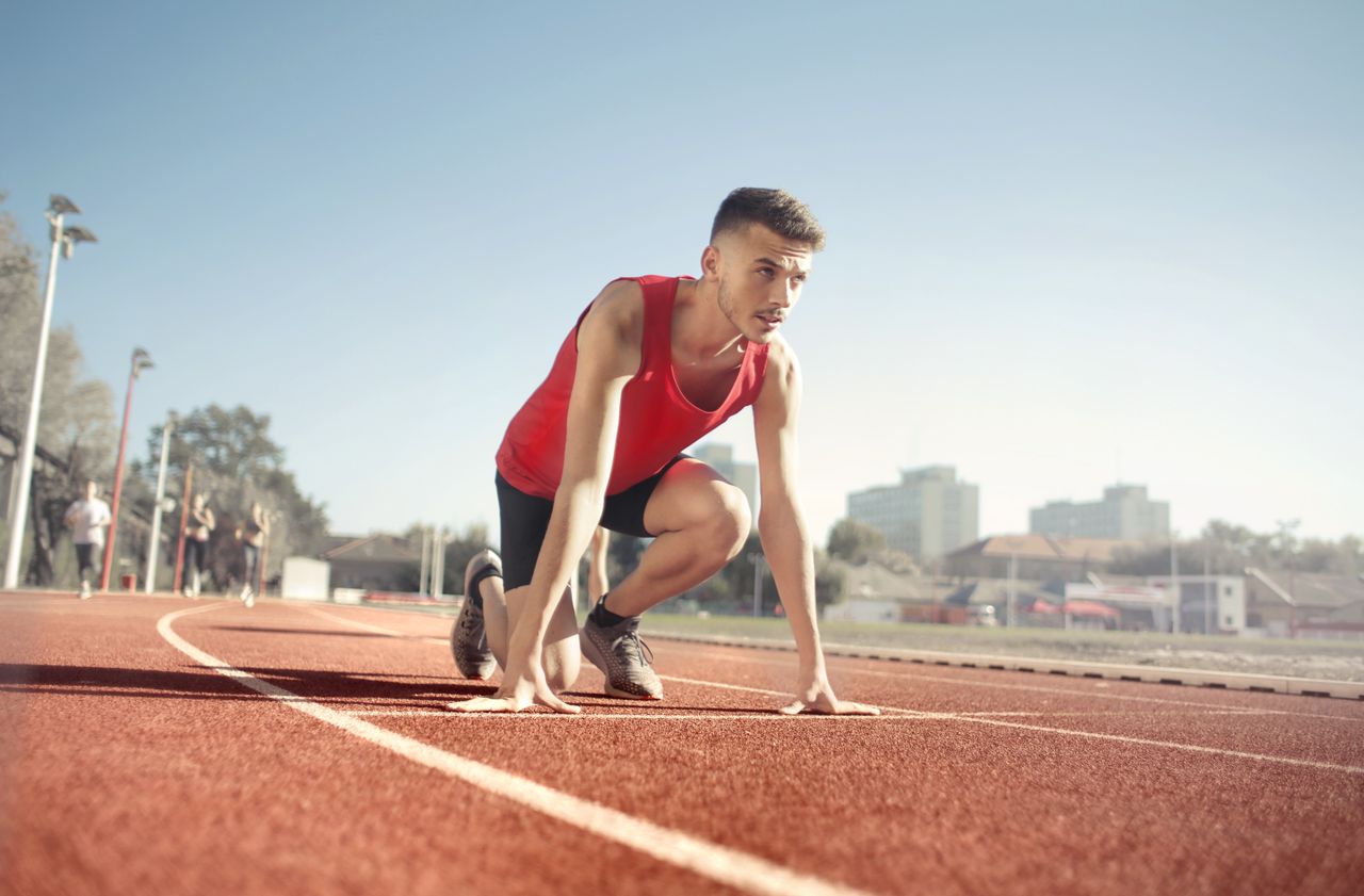 gallery-04 Young male athlete in start position on outdoor track, ready to sprint.