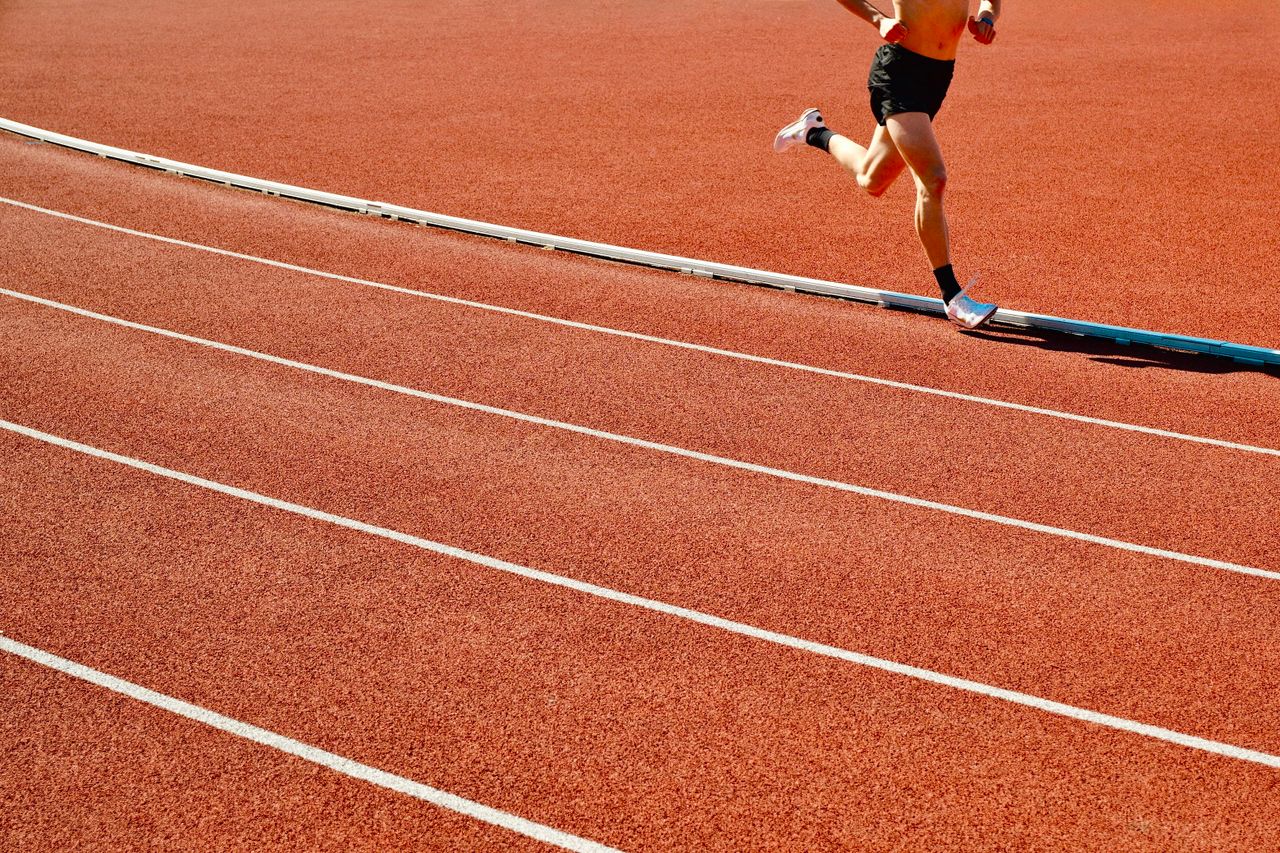 services-02 Athlete running on a red track in an outdoor stadium on a sunny day.